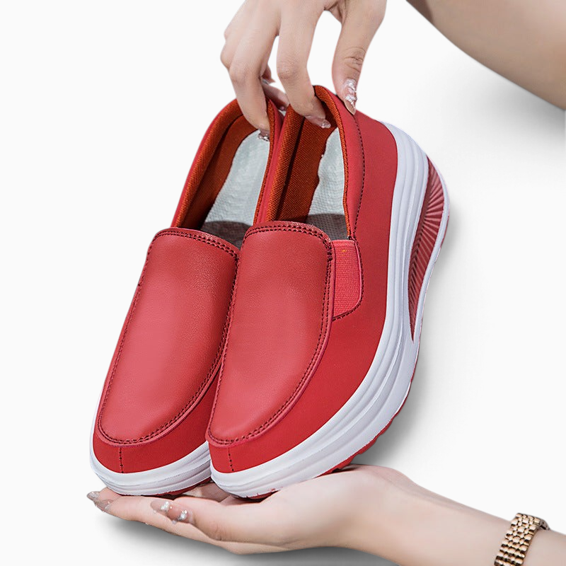 Mains tenant une paire de mocassins Orthopodys, marque exploitée par AIIBORI (SASU), rouges compensés à enfiler.